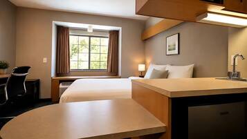 A hotel room with a bed, desk, chair, lamp, window with curtains, and a sink.