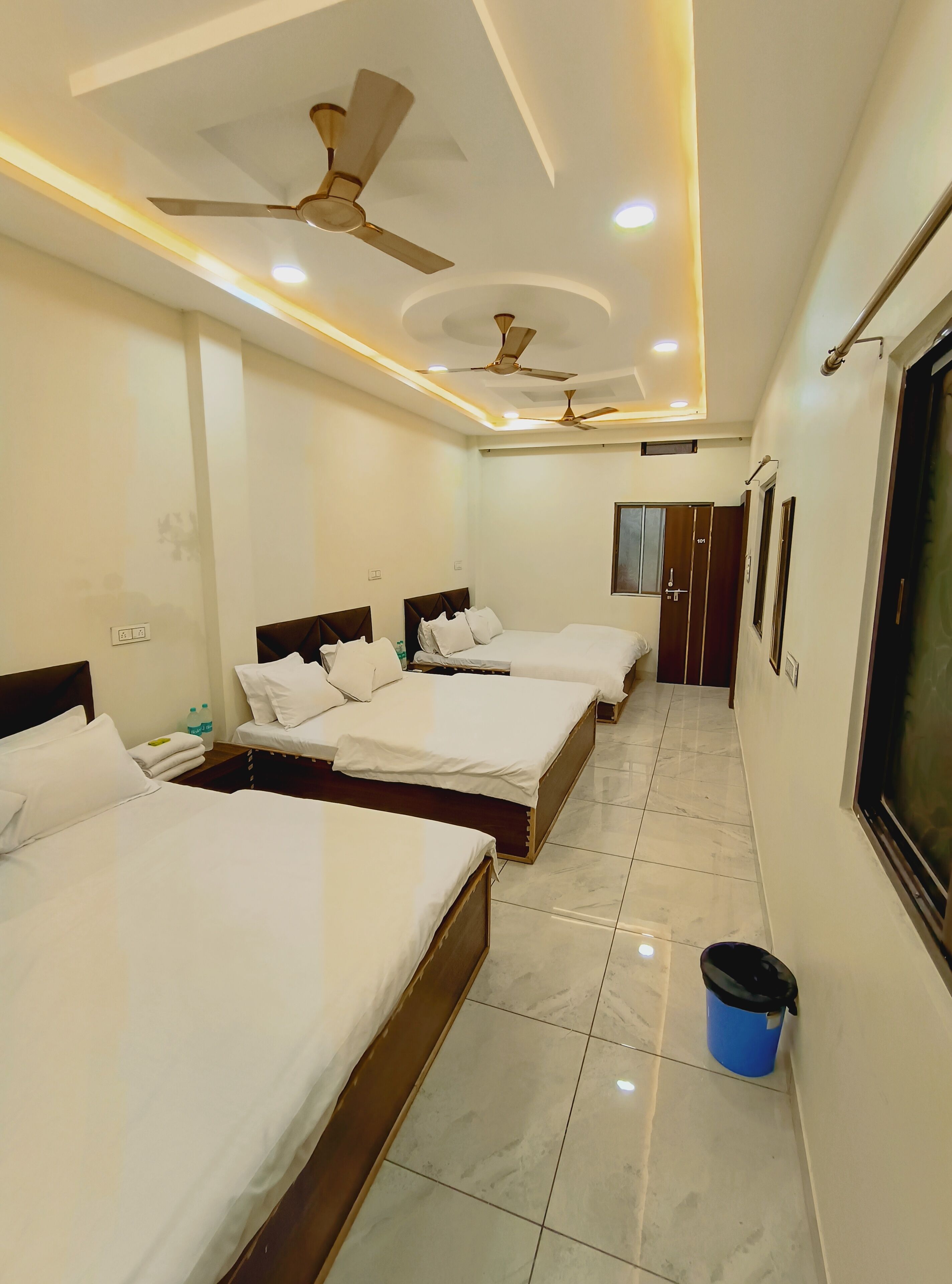 A hotel room with four beds, ceiling fans, recessed lighting, a tiled floor, and a trash bin.