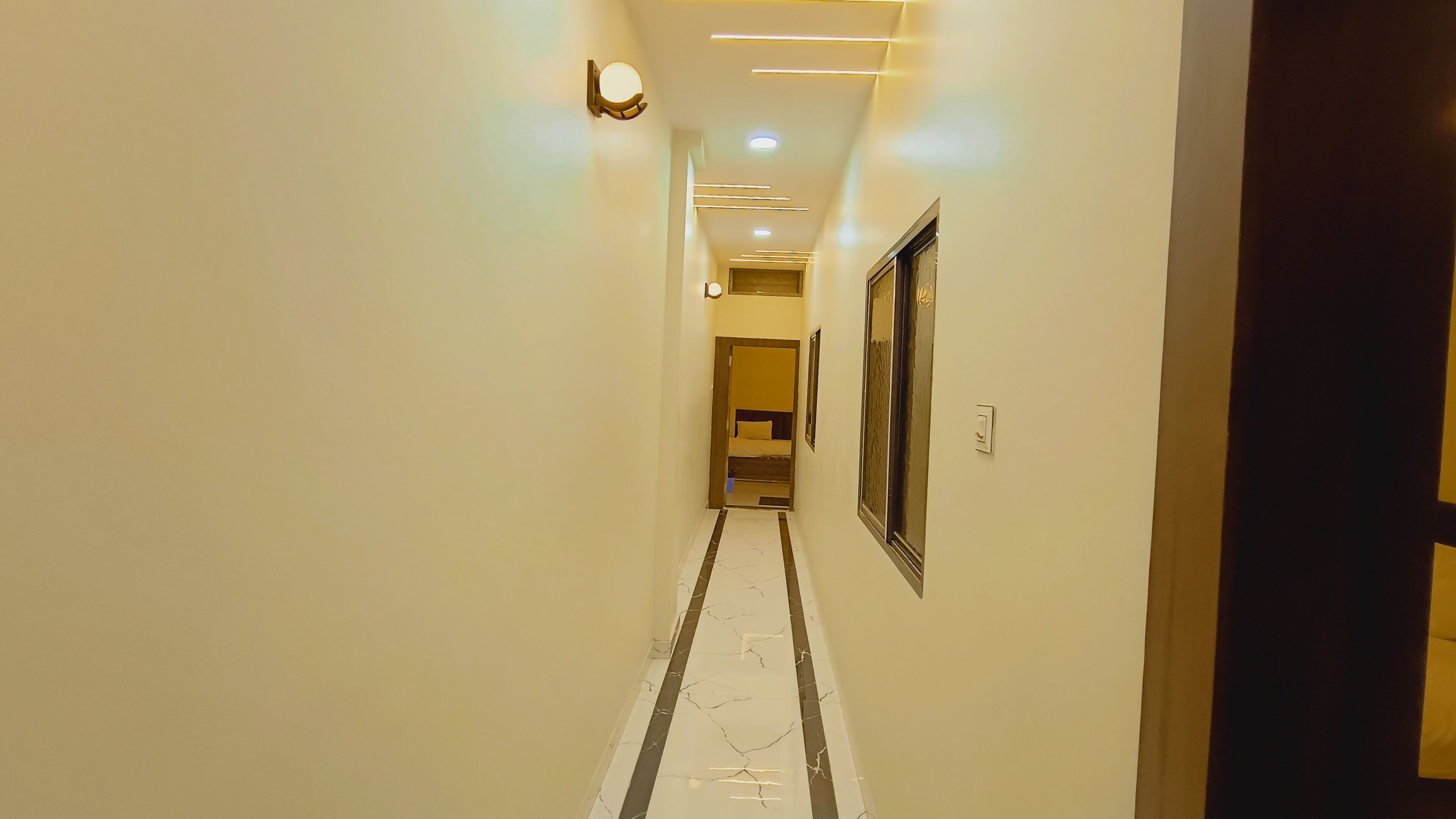 Un pasillo con piso de mármol, iluminación empotrada y una puerta a la derecha.