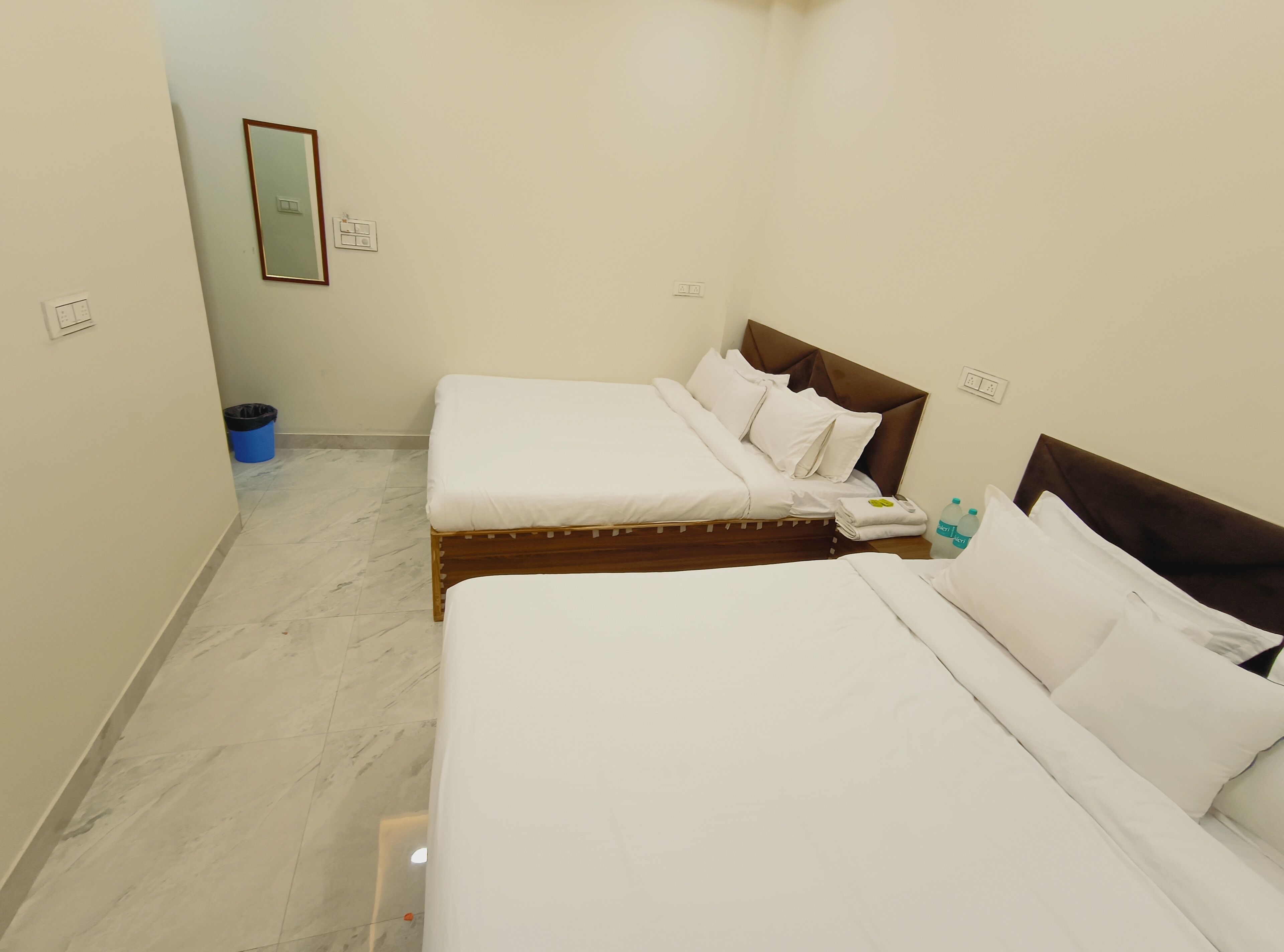 Una camera d'albergo con due letti, uno specchio e un cestino della spazzatura blu.