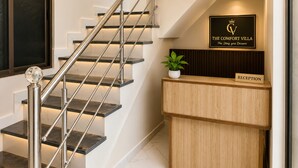 A reception desk with a sign reading 'The Comfort Villa,' a staircase with metal railings, and a potted plant.