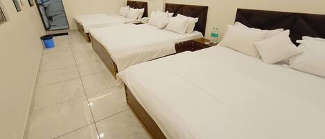 A hotel room with three beds, a blue trash bin, and a water bottle on the nightstand.