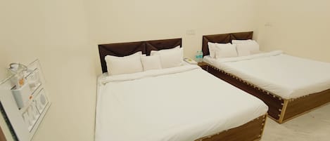 A hotel room with two beds, a bedside table, a wall-mounted light switch, and a small shelf with toiletries.