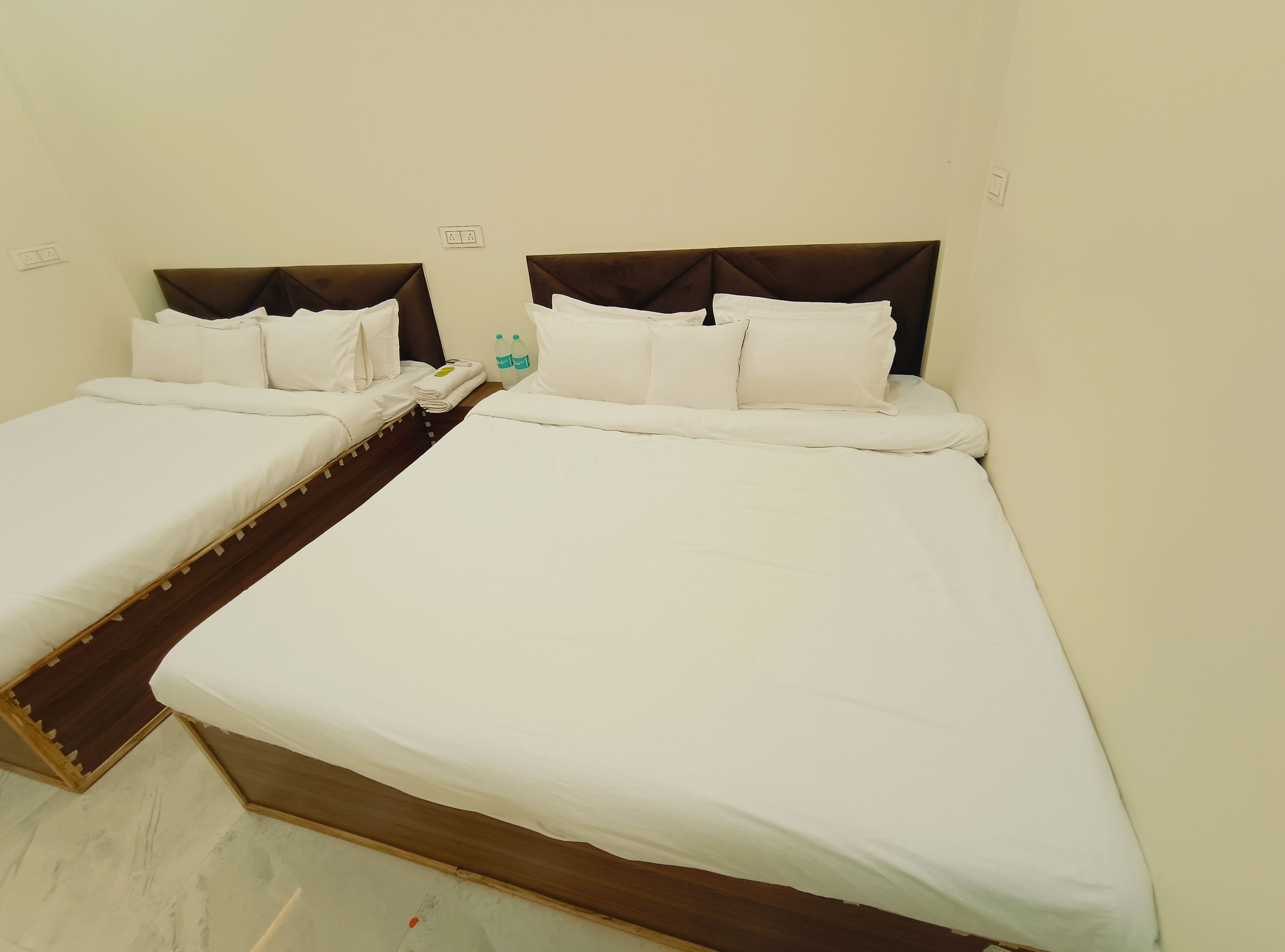 A hotel room with two single beds, a wooden floor, and a small table with a bottle of water.