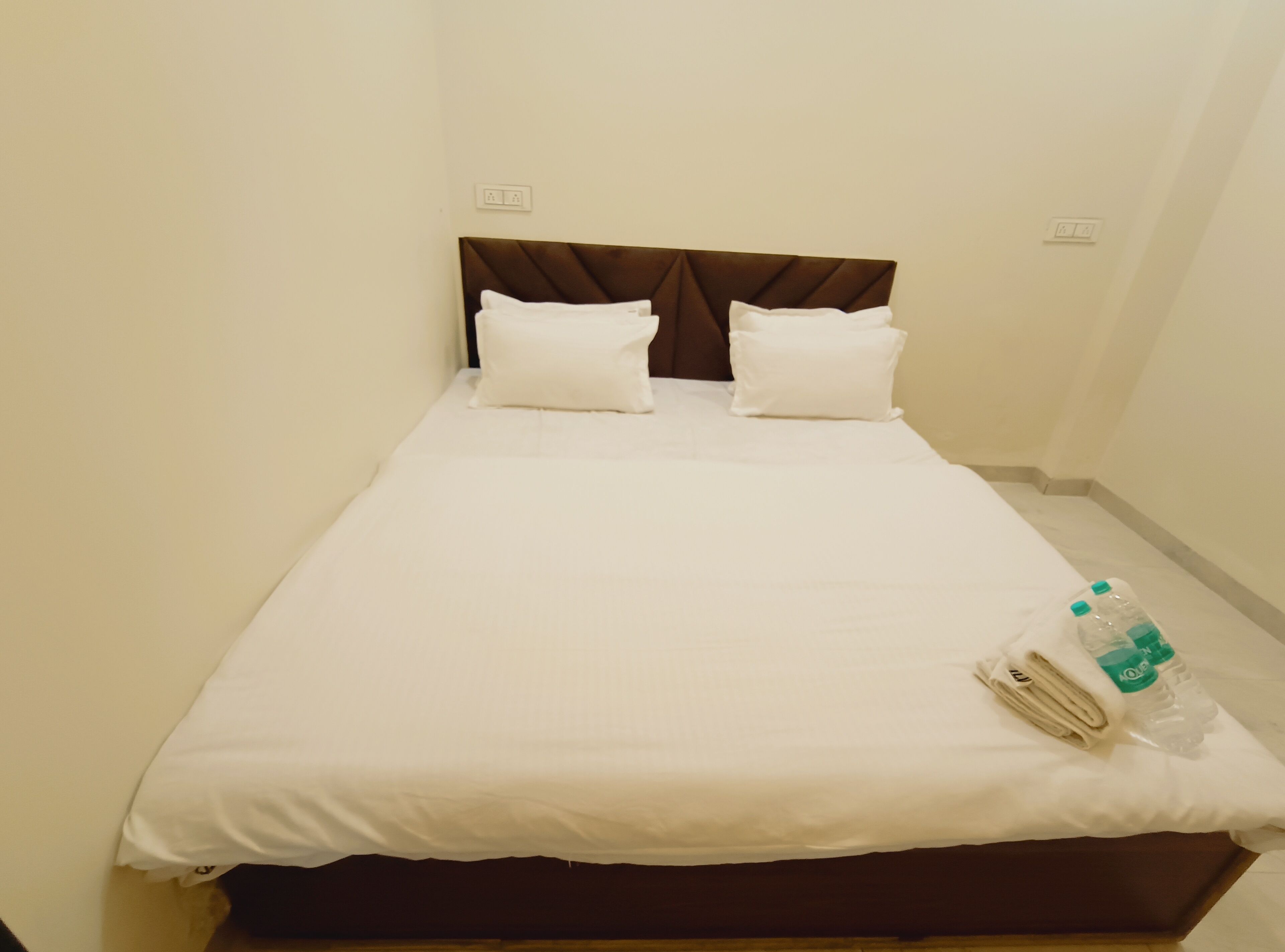 A neatly made bed with white linens and pillows, a brown headboard, and a folded towel on the side.