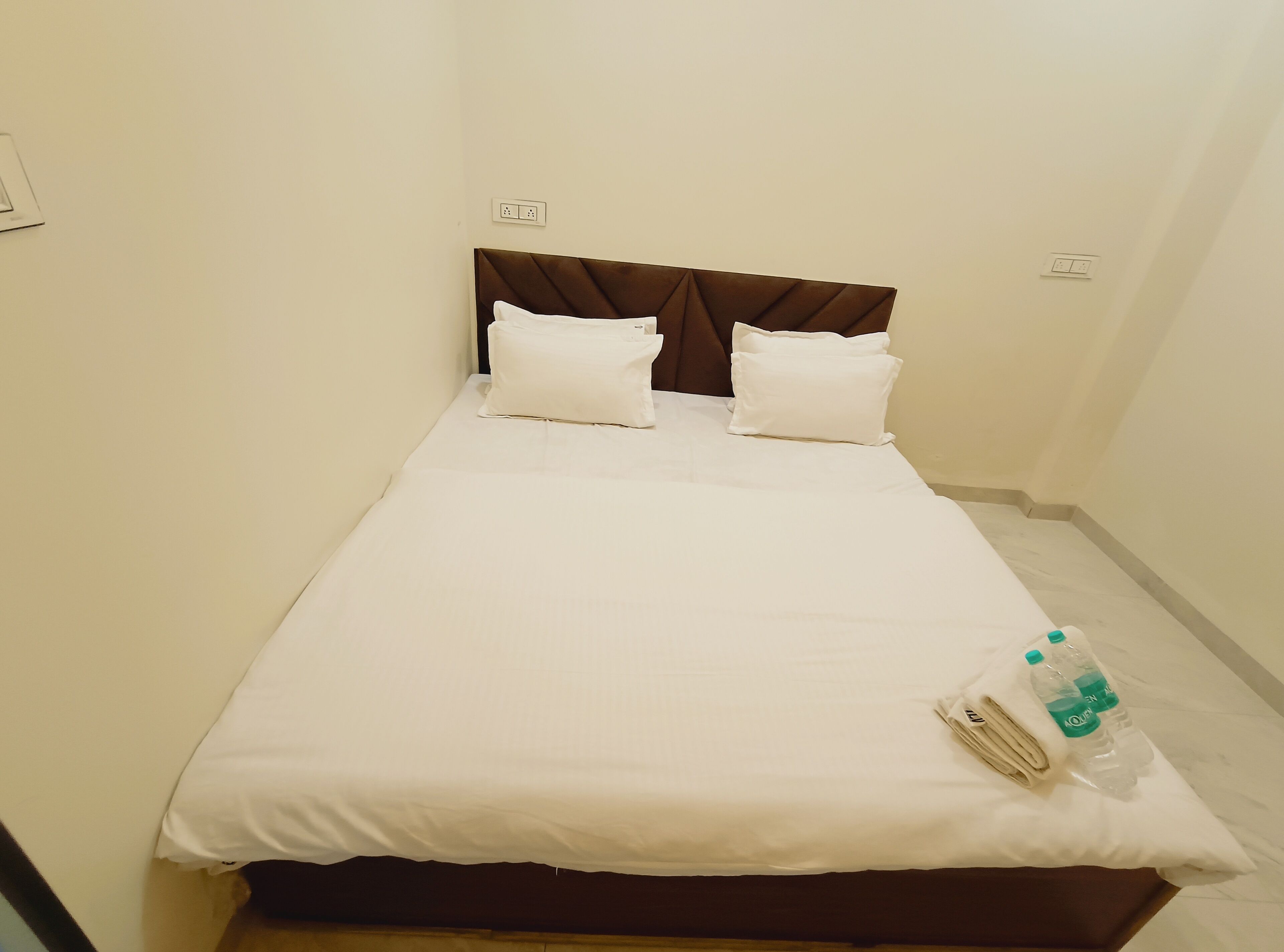 Una cama individual con cabecera marrón, ropa de cama blanca y una botella de agua al lado.