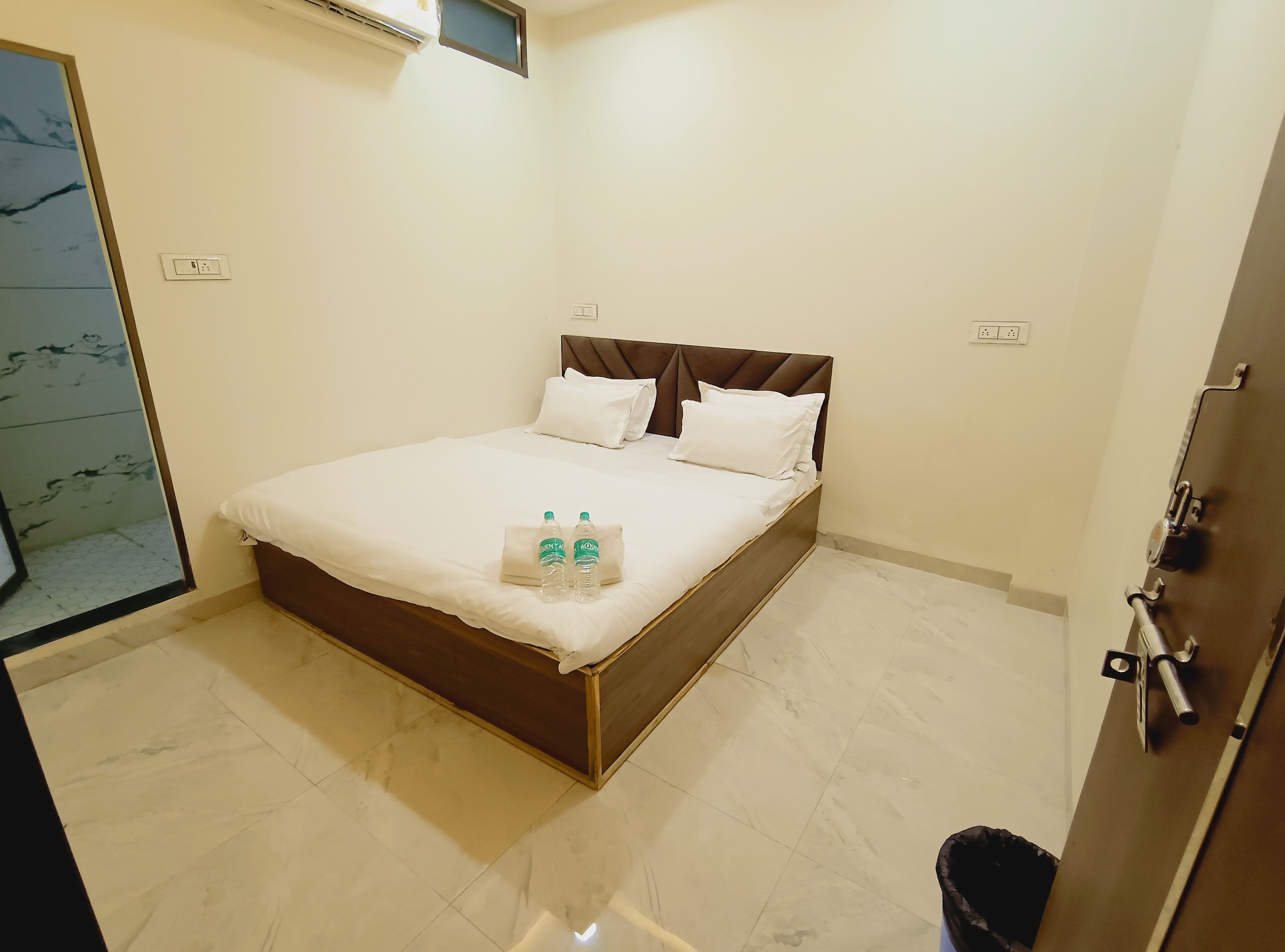 Une chambre d’hôtel avec un lit, une porte de salle de bain et une poubelle.