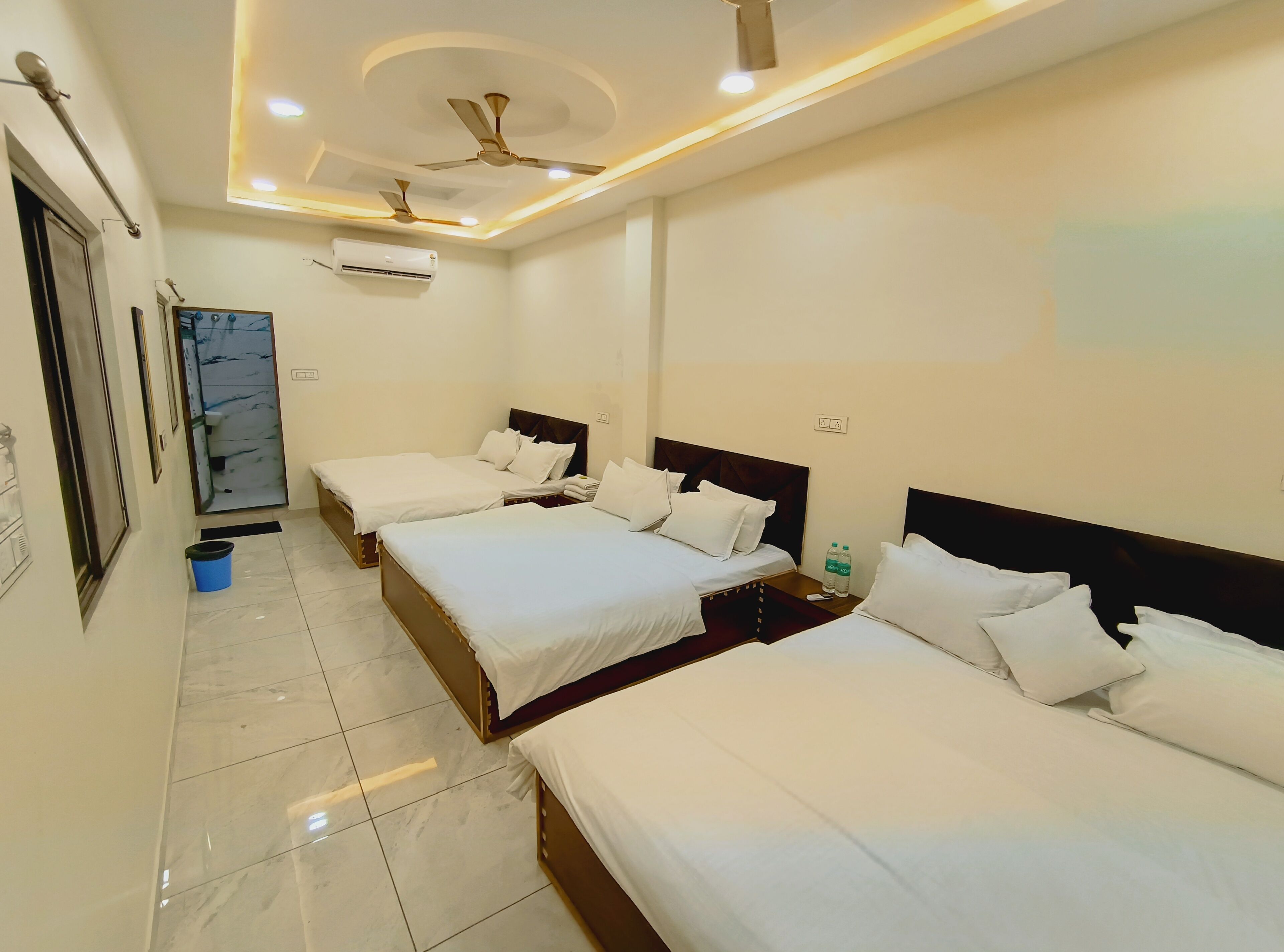 A hotel room with three beds, a ceiling fan, recessed lighting, an air conditioning unit, and a tiled floor.