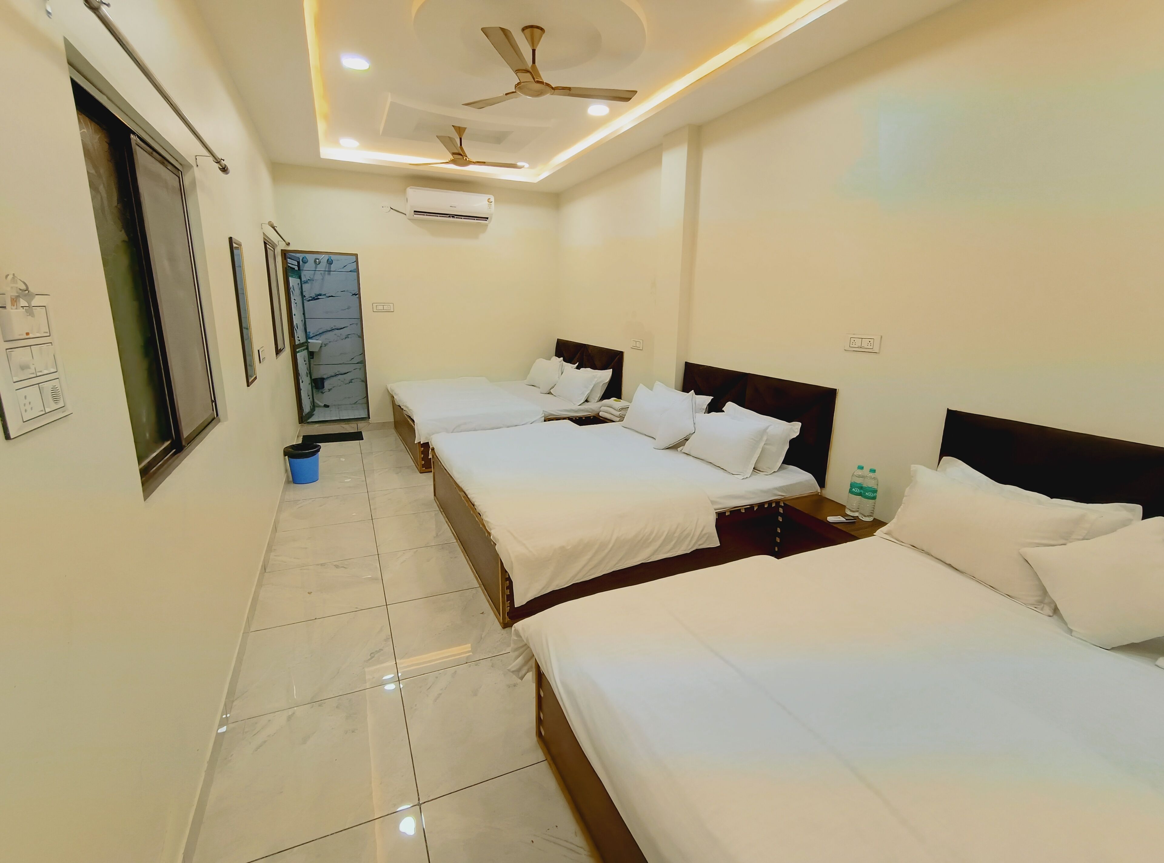A hotel room with three beds, ceiling fans, an air conditioning unit, and a tiled floor.