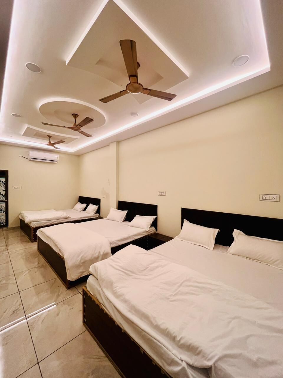 A hotel room with three single beds, ceiling fans, recessed lighting, and a tiled floor.