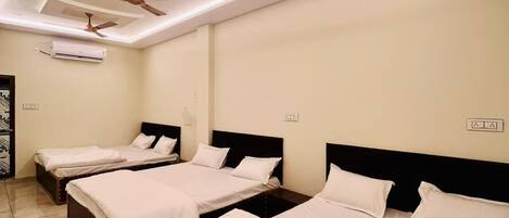 A hotel room with three single beds, ceiling fans, recessed lighting, and a tiled floor.