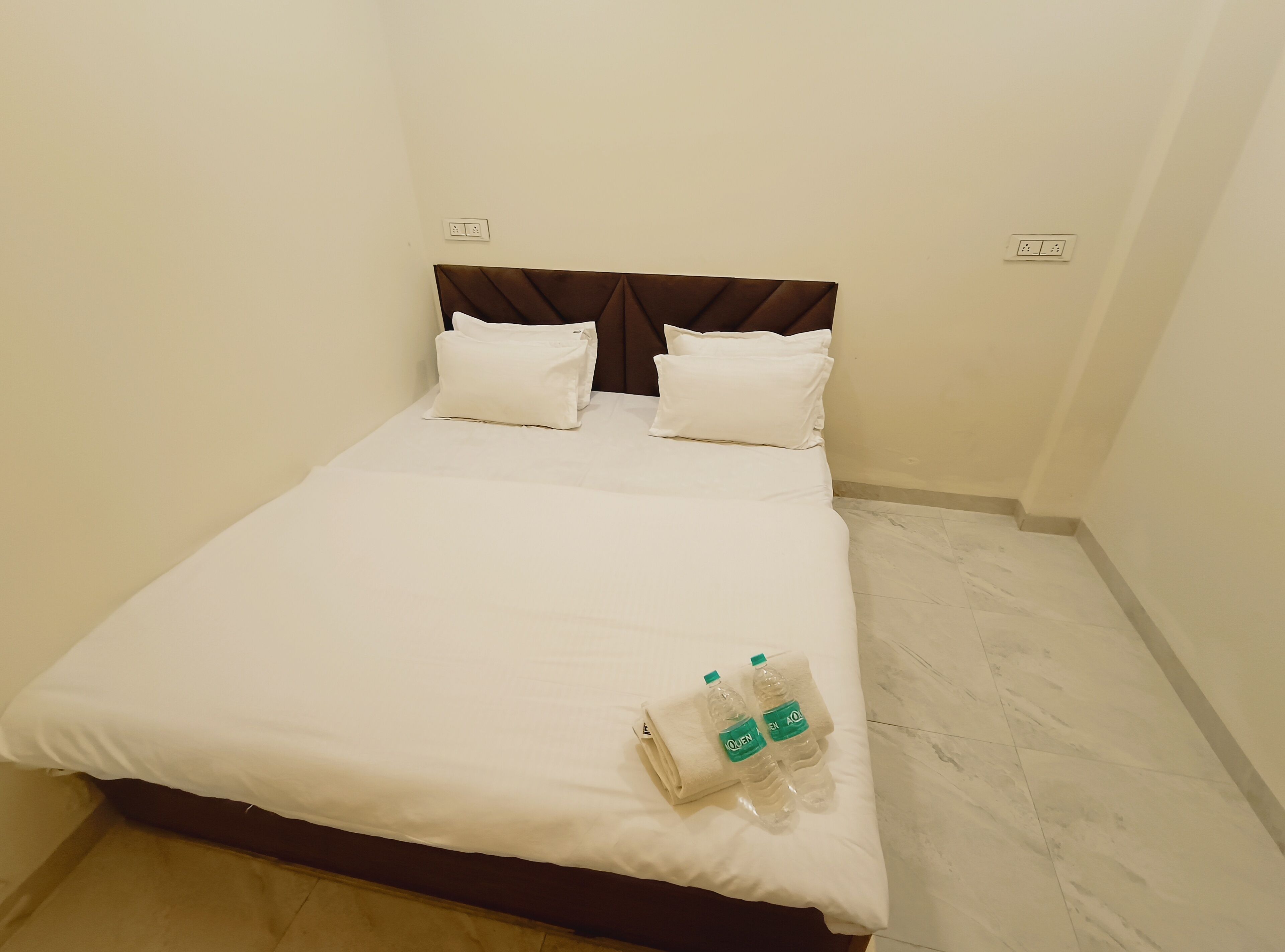 A neatly made bed with white linens, two pillows, and two bottles of water on the bed.