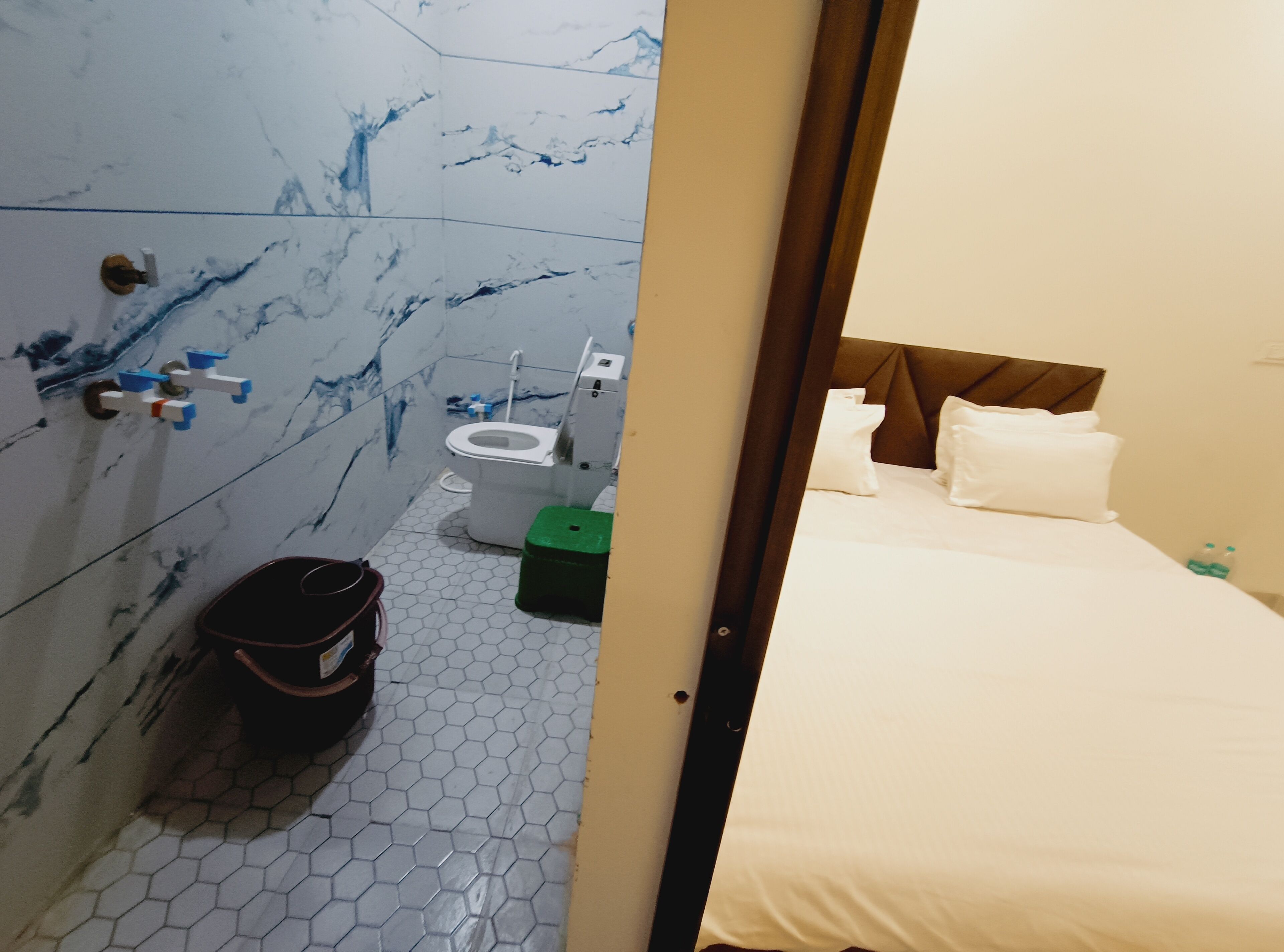 Une chambre d’hôtel avec salle de bain, un lit avec du linge de lit blanc et une poubelle verte.