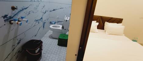 A hotel room with a bathroom, a bed with white linens, and a green trash bin.