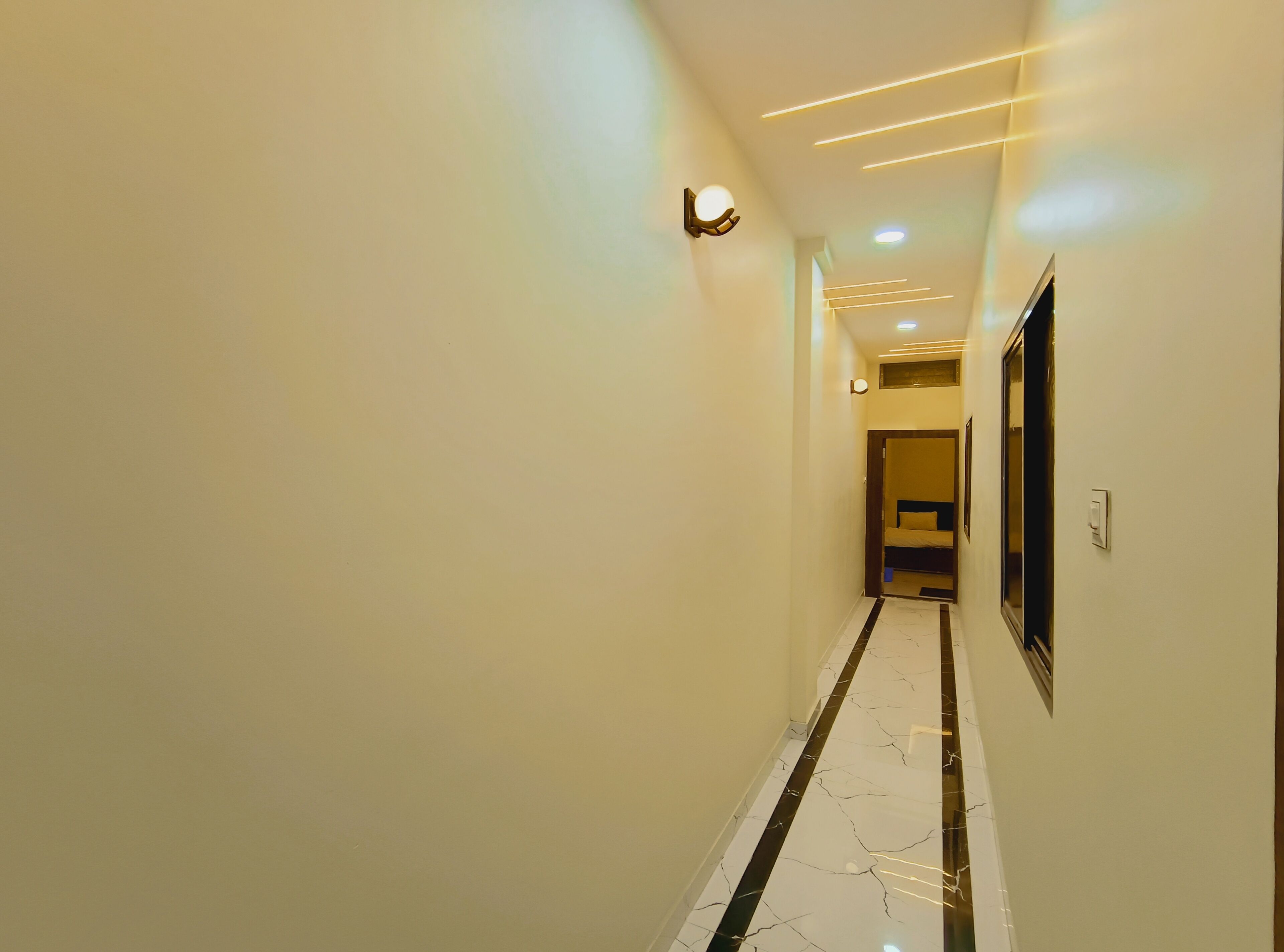 A hallway with a marble floor, recessed lighting, and a mirror on the wall.