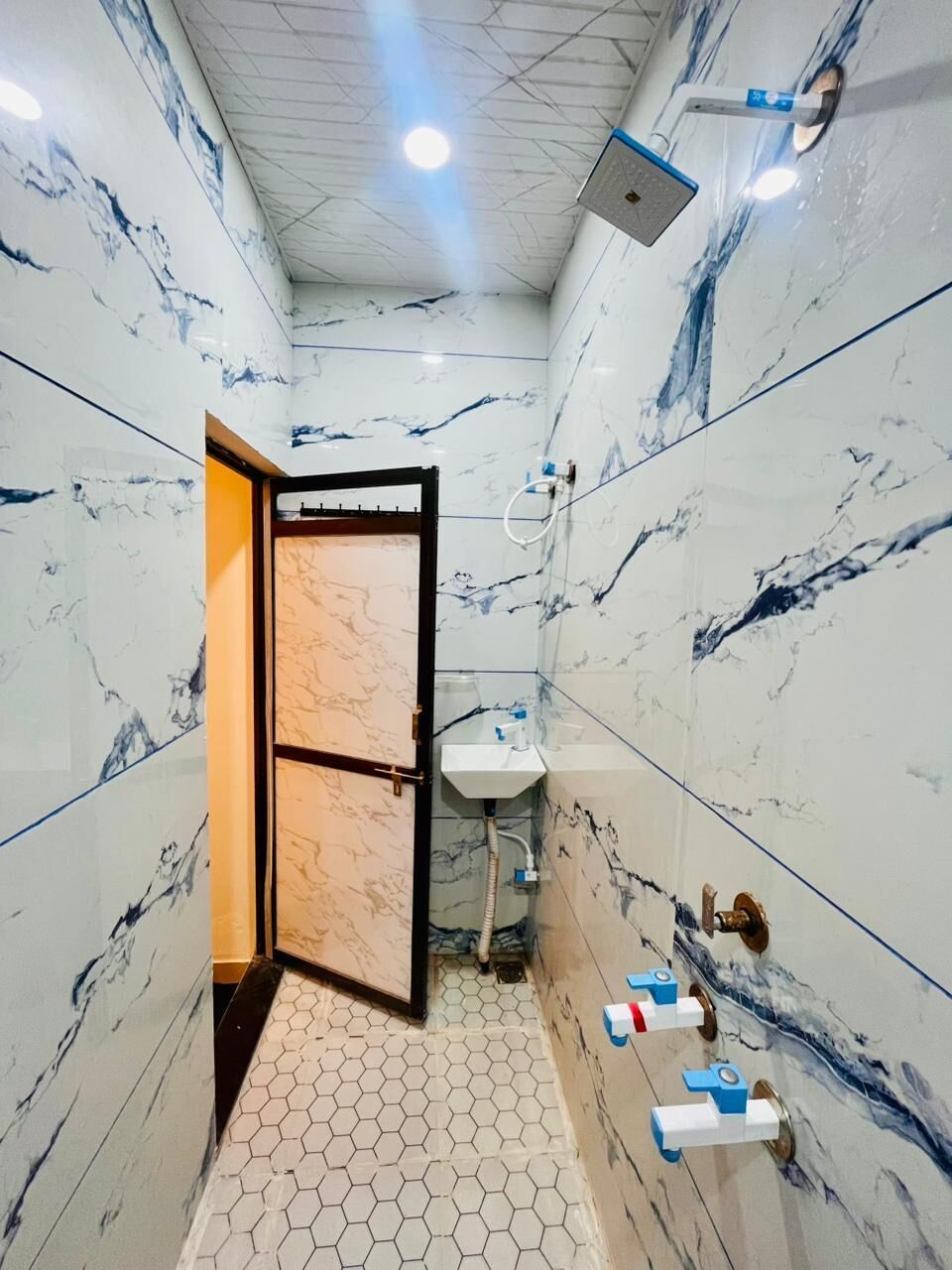 A bathroom with marble walls, a hexagonal floor pattern, a sink, and a shower.