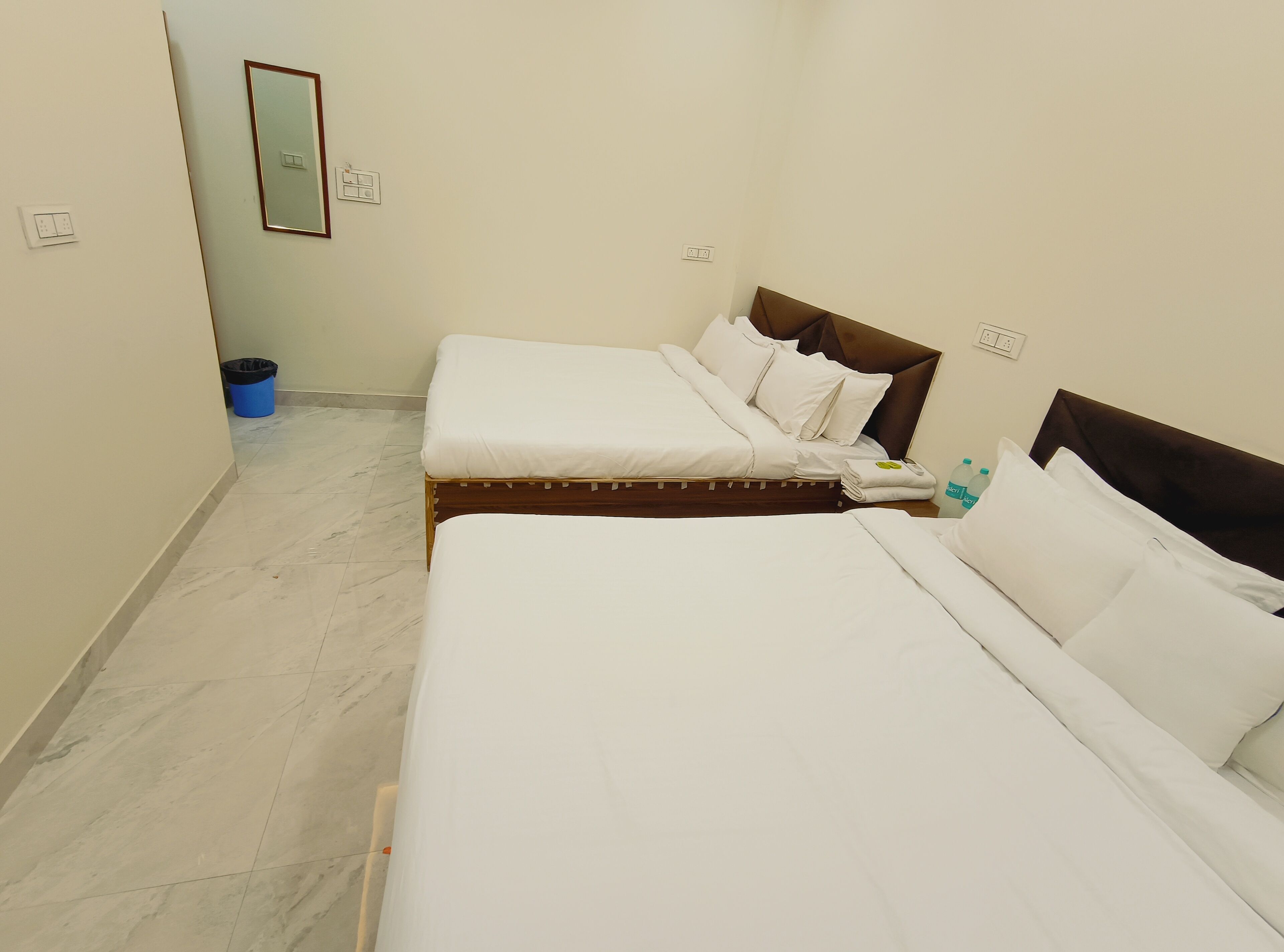 A hotel room with two beds, a mirror, and a trash bin.