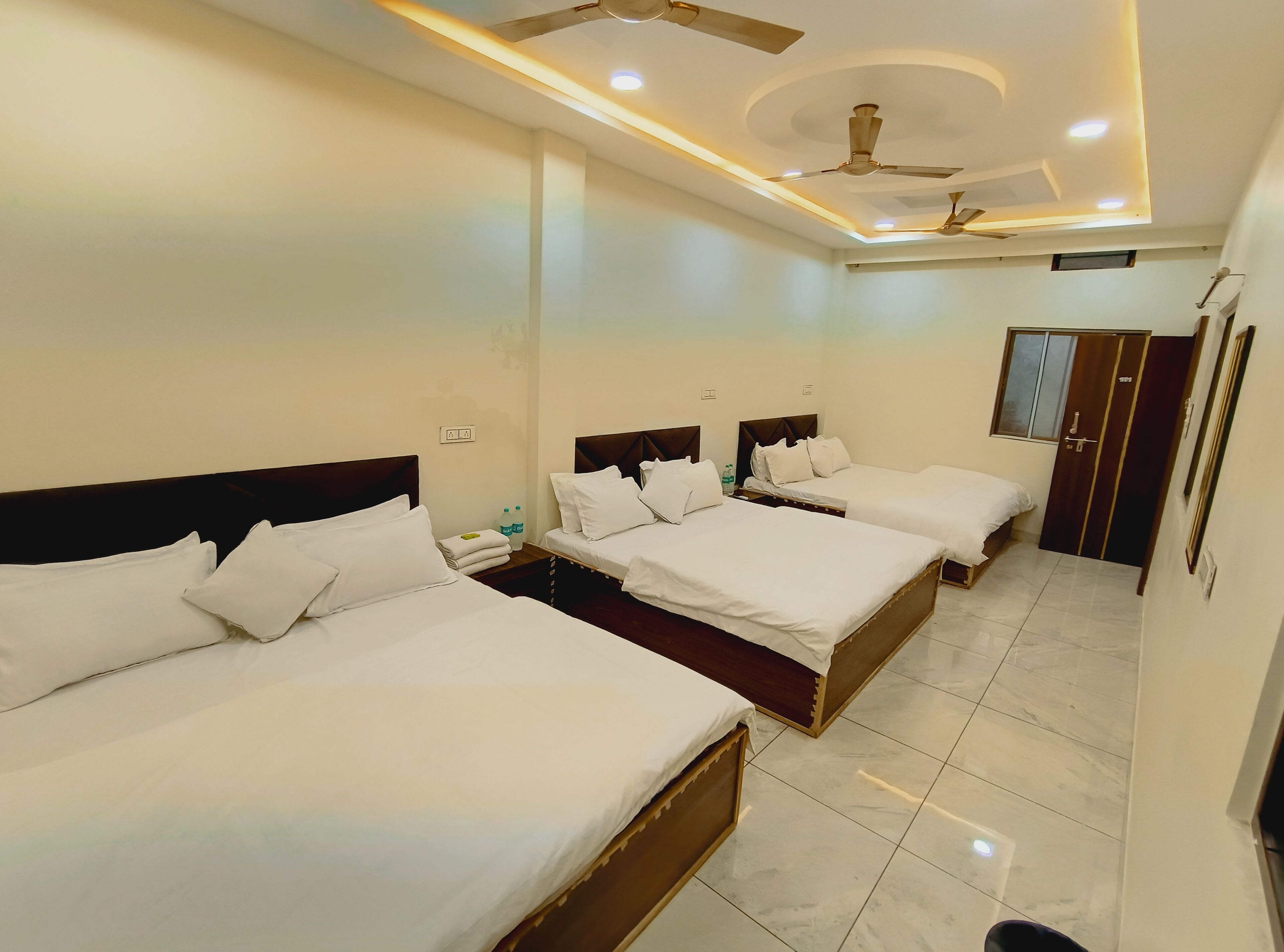 A hotel room with three beds, ceiling fans, recessed lighting, and a tiled floor.