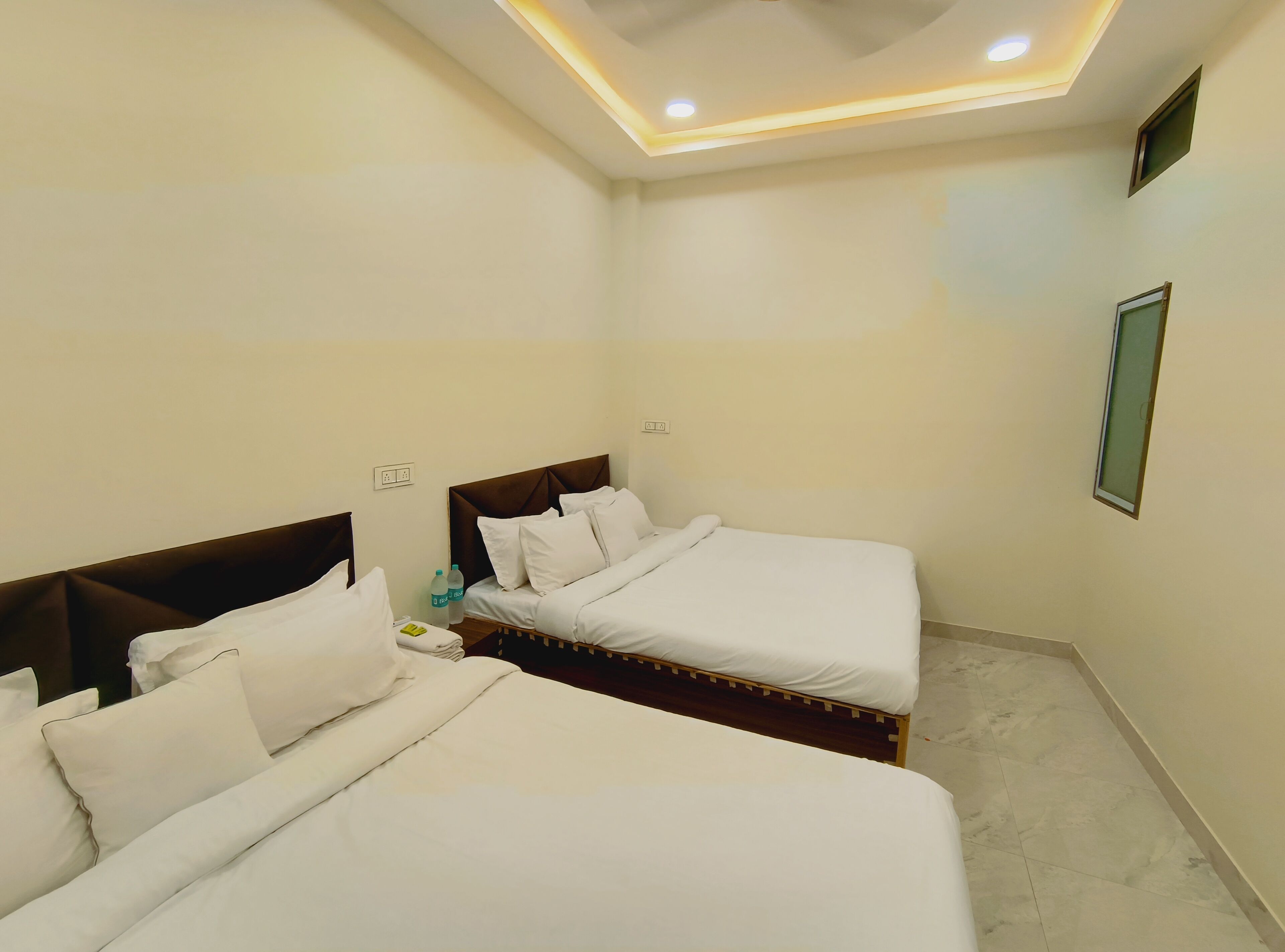 Une chambre d’hôtel avec deux lits, un luminaire au plafond et une petite fenêtre.