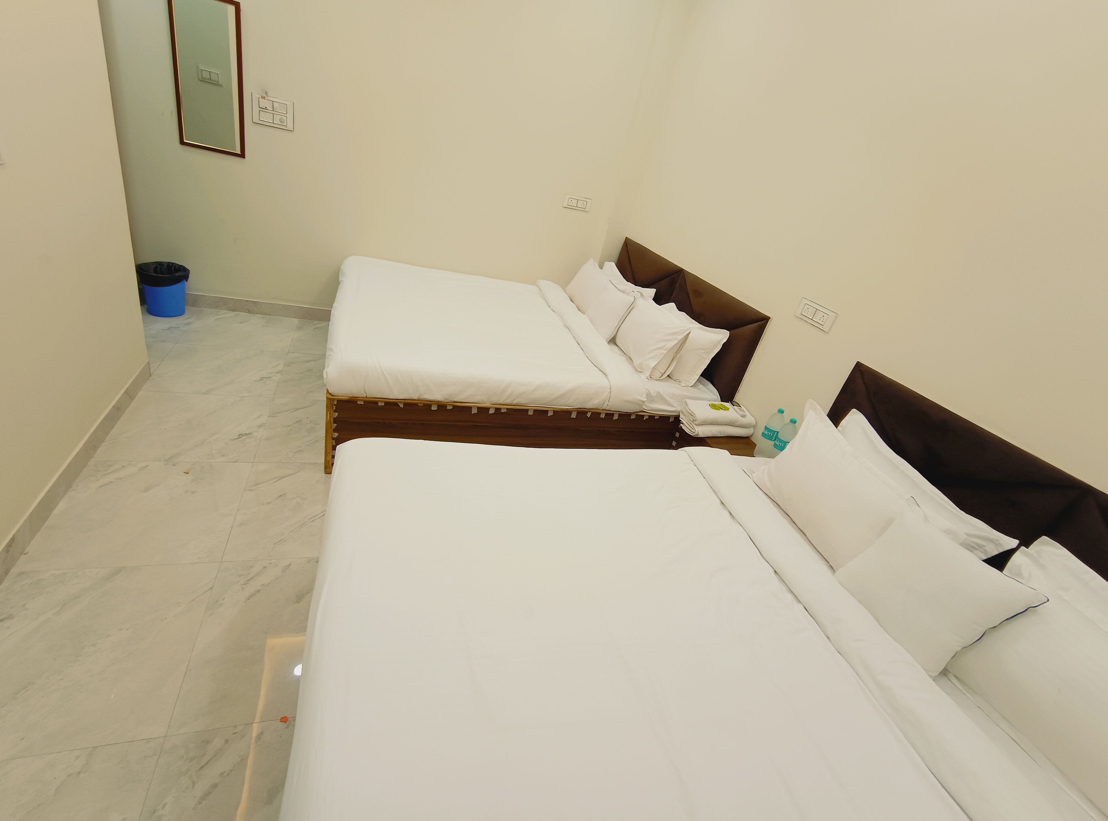 A hotel room with two beds, a blue trash bin, and a mirror on the wall.
