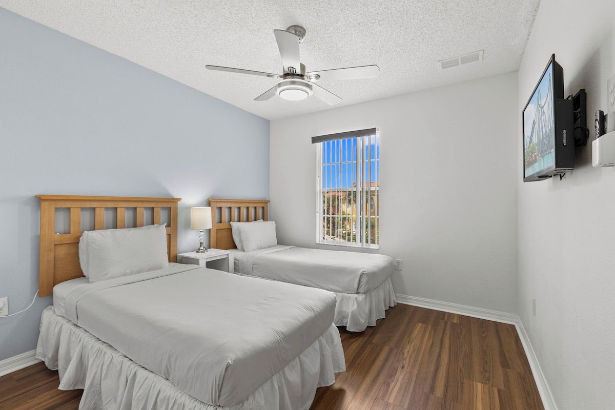 A bedroom with two beds, a ceiling fan, a window with a view, and a mounted TV.