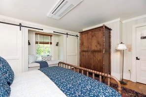 Ein Schlafzimmer mit einem Bett, einem Holzschrank, einem Fenster mit Jalousien und einer Stehlampe.