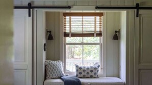 A room with a built-in bench seat, a window with blinds, and two wall-mounted lamps. - Blue Ridge Getaway (Roseland)