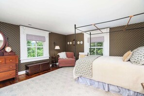 Une chambre à coucher avec un lit à baldaquin, une commode, une chaise et une fenêtre donnant sur un paysage verdoyant.