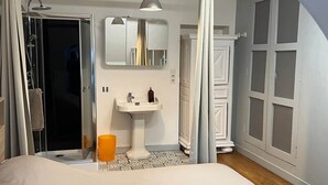 A bedroom with a large bed, a bathroom with a sink and mirror, and a shower.