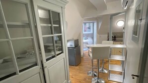 A narrow kitchen with wooden flooring, white cabinetry, and a small dining area with stools.