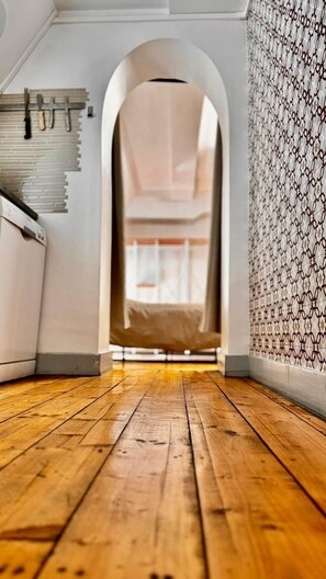An arched doorway leading to a room with a sloped ceiling, wooden flooring, and patterned wallpaper.