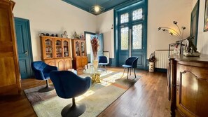A room with a wooden cabinet, a blue chair, a wooden table, and a window with blue shutters.