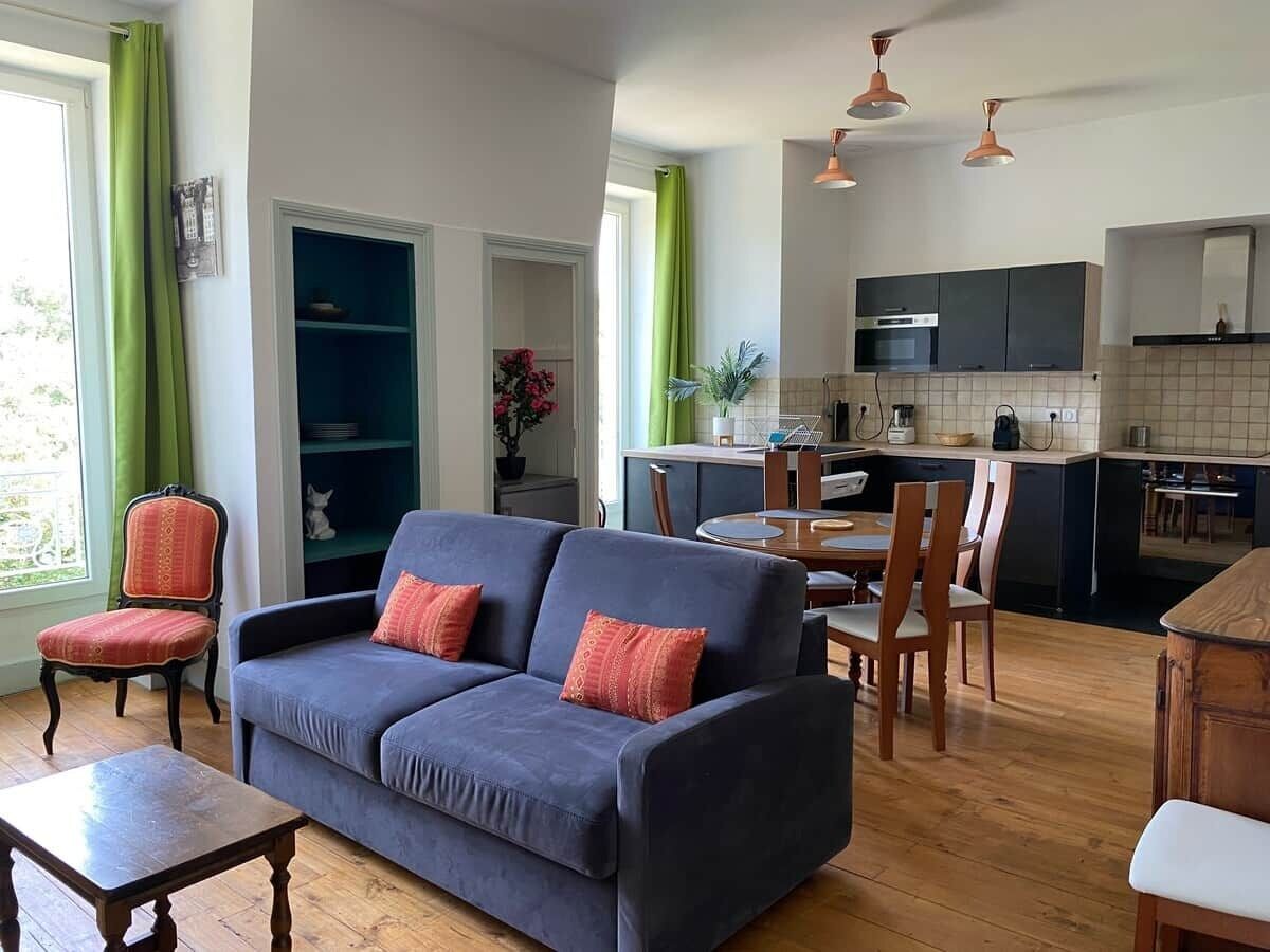 Una sala de estar con sofá, sillas, una mesa de comedor y una cocina con armarios y electrodomésticos.