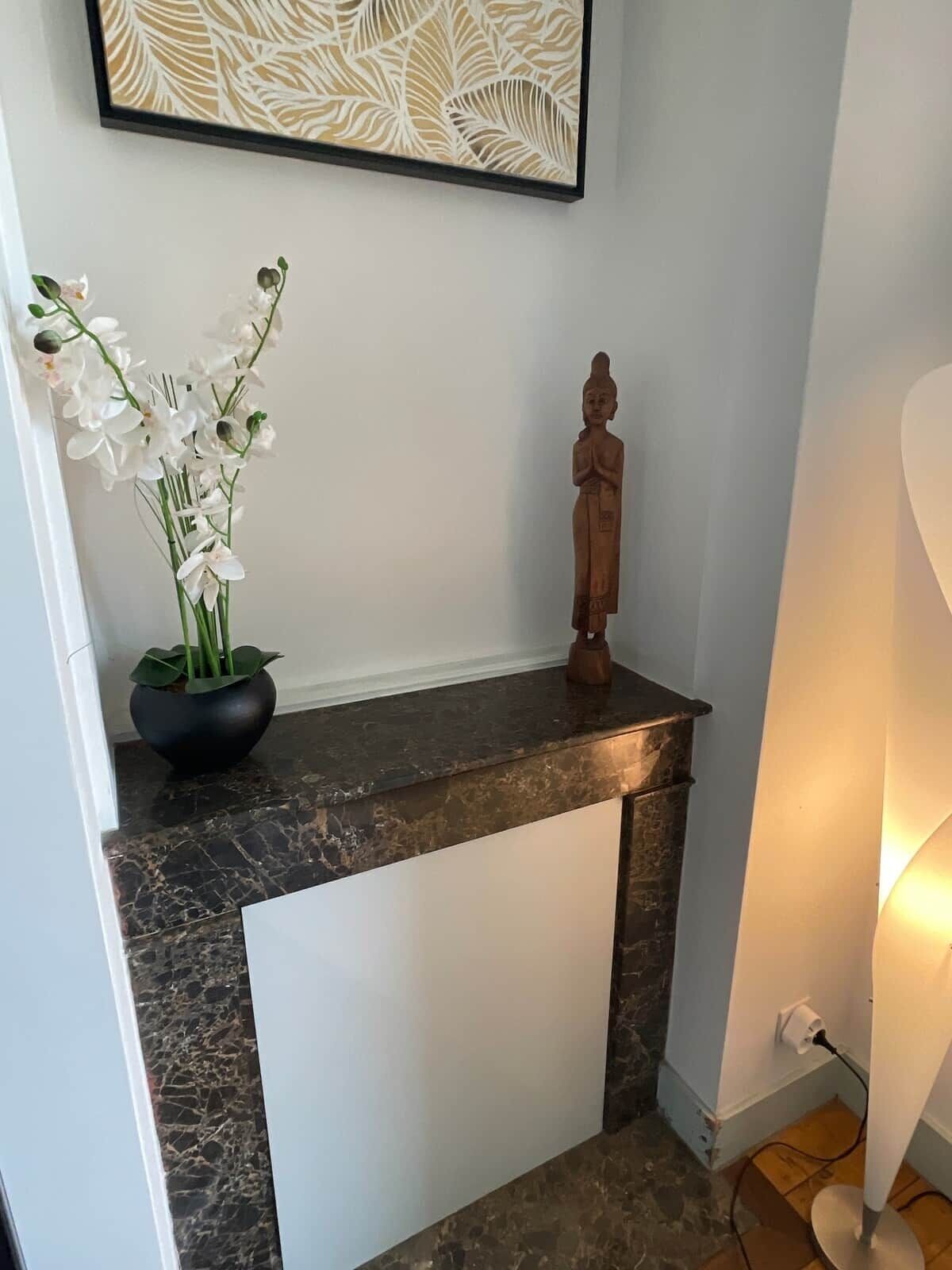 Une pièce avec un comptoir en marbre, une statue, une œuvre d’art encadrée et une plante en pot.