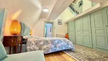 A bedroom with a bed, a nightstand, a lamp, a window, and a door leading to a staircase.