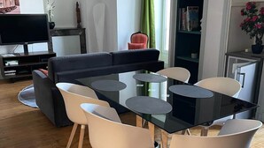 A modern living room with a black sofa, a glass dining table, and white chairs.