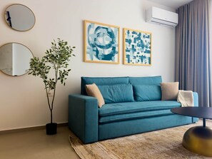 Ein modernes Wohnzimmer mit einem türkisfarbenen Sofa, zwei Wandspiegeln, abstrakter Kunst, einer Topfpflanze und einer Klimaanlage.