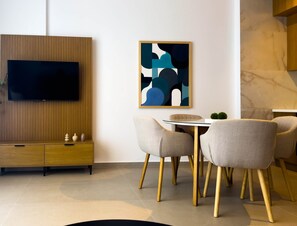 Ein modernes Wohnzimmer mit Flachbildfernseher, einer Holzkommode, einem runden Esstisch mit Stühlen und abstrakter Wandkunst.