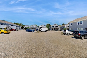 A parking lot with several cars and a van, surrounded by residential-style buildings with balconies. - Moon Tide - Bayside Beach Access & Parking (Provincetown)