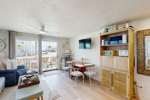 Una sala de estar moderna con un sofá, una mesa de comedor, sillas, un ventilador de techo y un televisor.