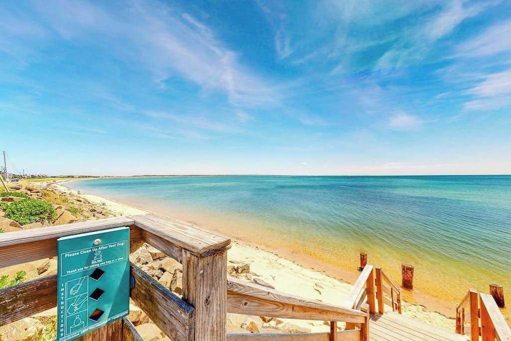 A beach with a wooden walkway and a sign instructing to clean up after dogs.