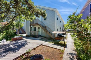 A two-story house with a wooden deck, a covered outdoor seating area, and a staircase leading to the entrance. - Moon Tide - Bayside Beach Access & Parking (Provincetown)