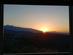 A sunset over a mountainous landscape with visible buildings and a clear sky.