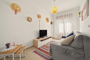 A modern living room with a sofa, TV, and a patterned rug. - Holiday Home 'A Casa Da Velha' with Private Terrace, Wi-Fi and Air Conditioning (Alvor)