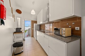A modern kitchen with white cabinets, a microwave, a toaster, and a sink. - Holiday Home 'A Casa Da Velha' with Private Terrace, Wi-Fi and Air Conditioning (Alvor)