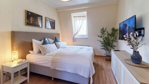 A bedroom with a bed, bedside table, lamp, window, and a television on a stand. - Spacious Central Apartment for 6 Guests in the Heart of Trier (Trier)