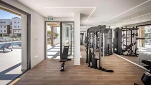 Ett gym med träningsutrustning, en bänk och utsikt över byggnader utanför.