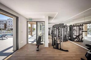 Una sala de gimnàstica amb equip d'exercici, una banca i vistes a edificis a l'exterior.