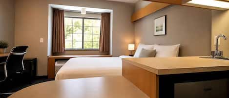 Habitación de hotel con cama, escritorio, silla, lámpara, ventana con cortinas y lavamanos.