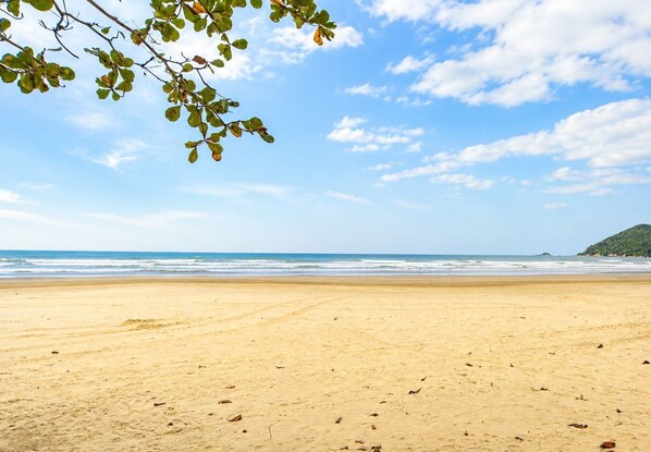 A beach with a clear sky, sandy shore, and a distant hill.